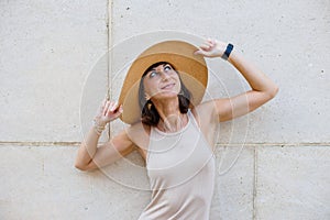 Young beautiful smiling girl in a trendy summer dress and hat posing near the wall on the street