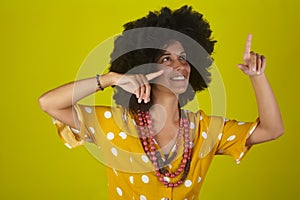 Young beautiful and smiling woman with curly afro hairstyle  pointing and looking up, indicating direction with fingers