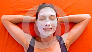 Young beautiful smiling woman with facial clay mask relaxing on the bed