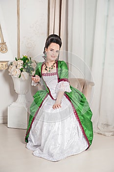 Young beautiful smiling woman in green rococo style medieval dress in the armchair