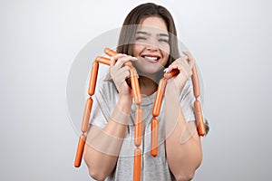 Young beautiful smiling woman holding meat sausages in both hands looks happy standing on  white background dietology and