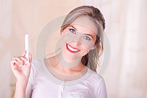 Young beautiful smiling woman holding a menstruation cotton tampon in her hand