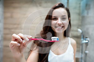 Young beautiful smiling woman holds tooth brush with tooth paste in the bathroom