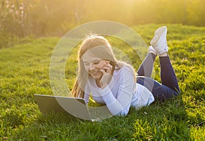 Young beautiful smiling woman with a laptop lies on the grass in