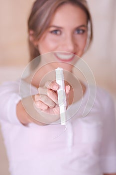 Young beautiful smiling woman pointing in front of her a menstruation cotton tampon, in a blurred background