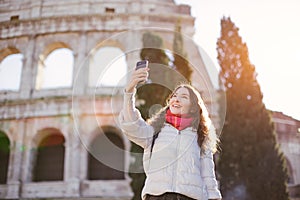 Young beautiful smiling woman posing against Roman colosseum and making selfie with smartphone