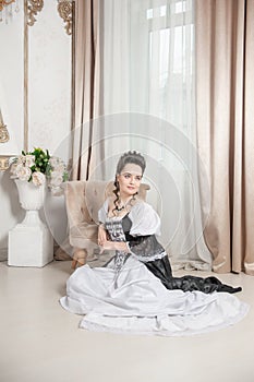 Young beautiful smiling woman in rococo style medieval dress sitting on the floor