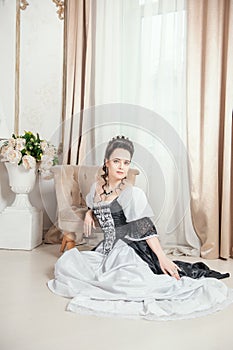 Young beautiful smiling woman in rococo style medieval dress sitting on the floor