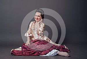 Young beautiful smiling woman in rococo style medieval dress sitting on the floor