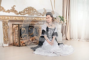 Young beautiful smiling woman in rococo style medieval dress sitting on the floor near fireplace