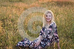 Young beautiful smiling woman sitting on grass in long dress