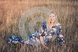 Young beautiful smiling woman sitting on grass in long evening dress