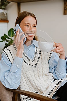 Young beautiful smiling woman talking phone sitting in armchair