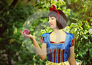 Young beautiful snow-white close-up keeps a red poisoned apple against the background of trees in the forest