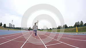 A young beautiful sport woman starts running at the city athletics track during a day training in slow motion 4K video