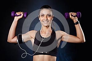 Young beautiful sportive girl training with dumbbells over dark background.
