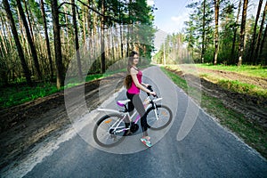 Young beautiful sports girl on a white bicycle in the woods