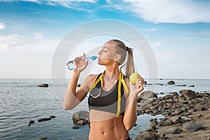 Young beautiful sportswoman drinking water on beach with measuring tape