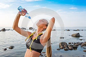 Young beautiful sportswoman drinking water on beach with measuring tape