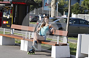 Young, beautiful, sporty and fit girl in inline skates.Sit on the bench.