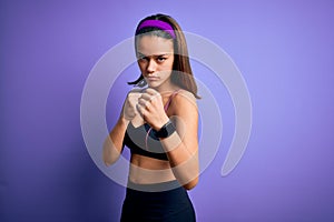 Young beautiful sporty girl doing sport wearing sportswear over isolated purple background Ready to fight with fist defense