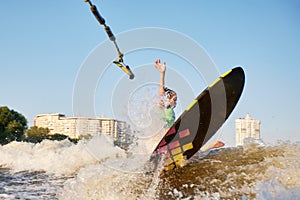 Young beautiful sporty girl in a green life jacket rides a wakeboard on a river or lake near city. Happy athlete girl