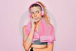 Young beautiful sporty woman with blue eyes wearing towel listening to music using headphones with hand on chin thinking about