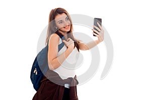 Young beautiful student girl with backpack makes selfie isolated on white background in studio