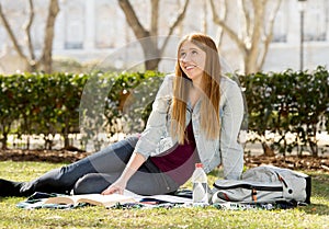 Young beautiful student girl on campus park grass with books studying happy preparing exam in education concept
