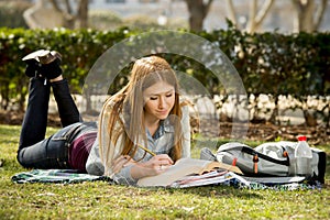 Young beautiful student girl on campus park grass with books studying happy preparing exam in education concept