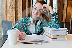 Young beautiful student girl is doing her homework or preparing to the exams siting with books copybooks