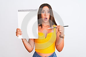 Young beautiful student girl holding notebook standing over isolated white background scared in shock with a surprise face, afraid