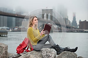 Young beautiful student girl reading a book sitting near New York City skyline