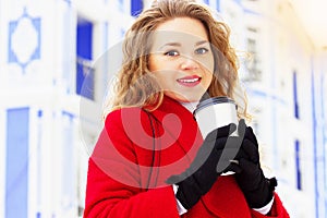 Young, beautiful and stylish blonde hair girl in red coat drinking coffee on the city street. Womens fashion.