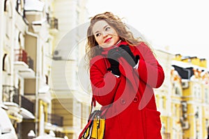 Young, beautiful and stylish blonde hair girl in red coat and with handbag walking through city streets. Womens fashion.