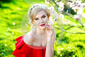 Young beautiful stylish girl in red summer dress walking and posing between trees at alley