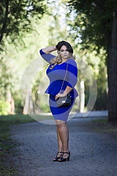 Young beautiful stylish plus size fashion model in blue dress outdoors, xxl woman on nature