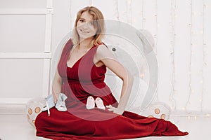 Young beautiful stylish pregnant woman in red long evening dress on white background of child room