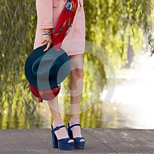 Young beautiful stylish woman walking down the street in a pink coat, floral scarf, hat in hand, in high shoes