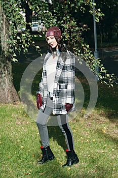 Young beautiful stylish woman, wearing a coat in a white and black cage, white jacket, gray trousers, black boots. Street style, s