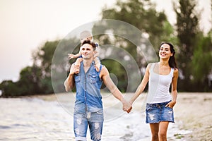 Young beautiful and stylishly dressed family of three people mom, dad and daughter of one year on the shoulders of a man walking a