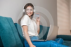 Young beautiful sucessful woman in headphones working in her laptop on the sofa in the living room looking very happy