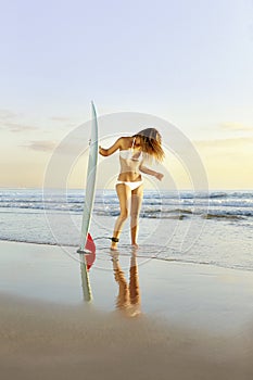 Young beautiful surfer girl standing on beach with surfboard