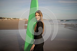 Young beautiful surfer woman with surfboard posing on sandy beach at sunset