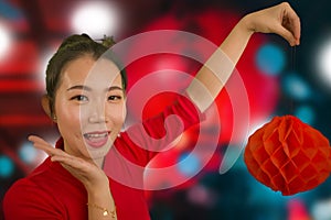 Young beautiful and sweet Asian Chinese woman in traditional bun hair style and red dress holding lantern celebrating New Year in