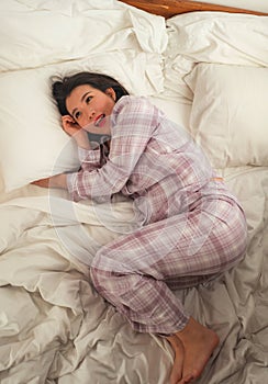 Young beautiful and sweet Asian Korean woman in bed feeling happy and relaxed wearing cute pajamas enjoying lazy Sunday morning at