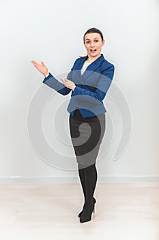 Young beautiful teacher standing, pointing at the copy space for text or product on her side, looking confused.