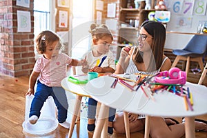 Young beautiful teacher and toddlers playing meals using plastic food and cutlery toy at kindergarten