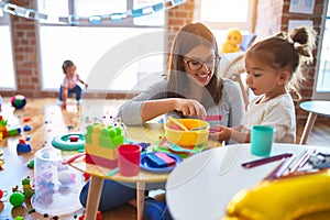 Young beautiful teacher and toddlers playing on the table with lots of toys at kindergarten