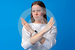 Young beautiful teen girl crossing arms doing negative sign on blue background